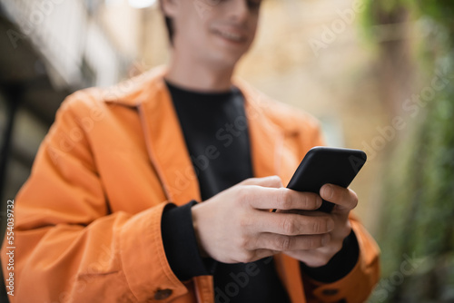 Cropped view of blurred man in jacket using smartphone outdoors.