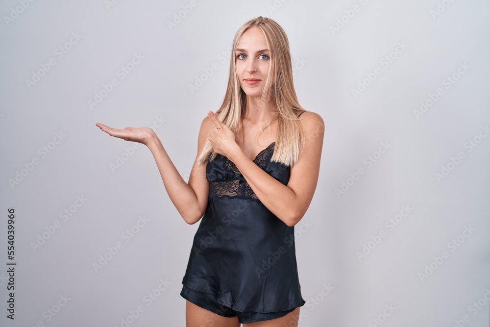Fototapeta premium Young caucasian woman wearing nightgown showing palm hand and doing ok gesture with thumbs up, smiling happy and cheerful