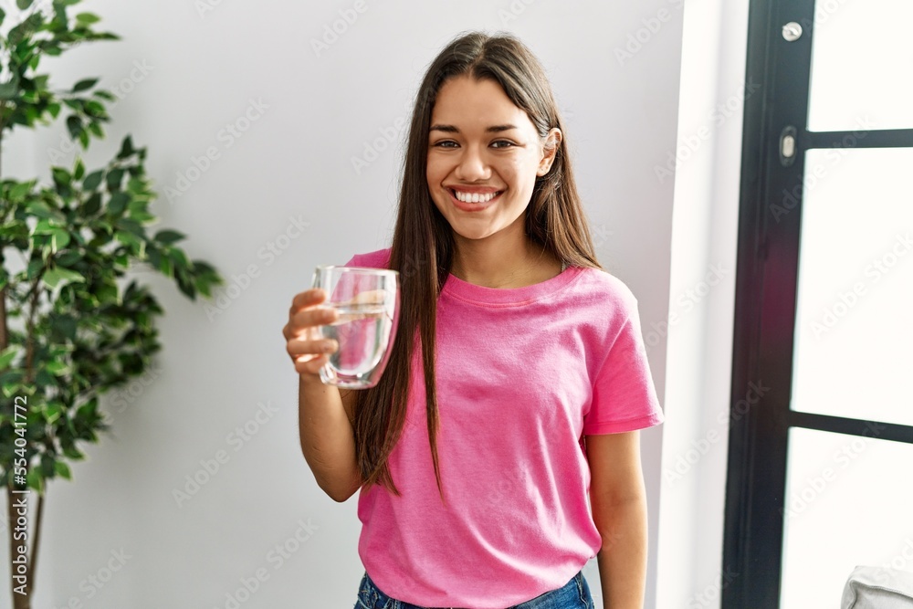 Young latin woman smiling confident drinking water at home