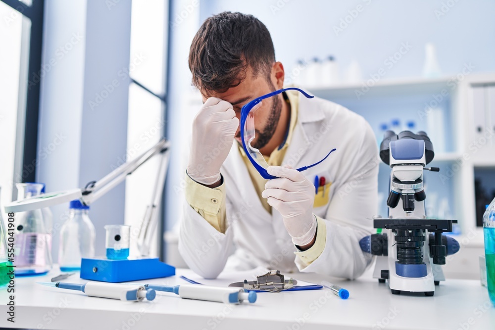 Fototapeta premium Young hispanic man wearing scientist uniform stressed working at laboratory