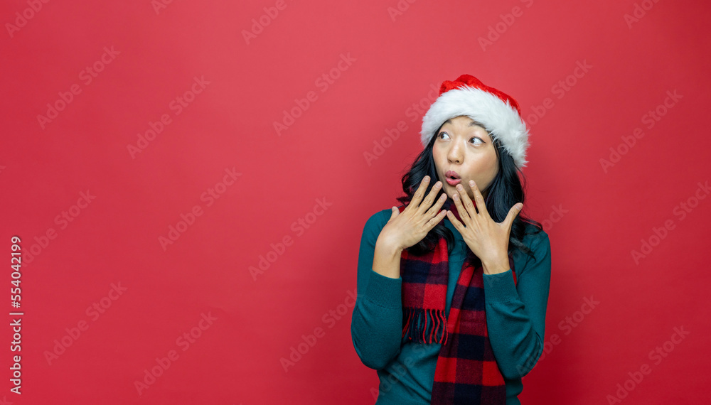 Pretty smiling asian woman in warm christmas sweater and santa hat is having excitement on red background for season celebration concept with copy space Pretty smiling asian woman in warm christmas sweater and santa hat is having excitement on red background for season celebration concept with copy space