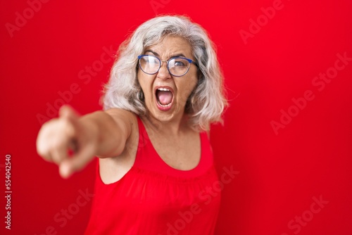 Middle age woman with grey hair standing over red background pointing displeased and frustrated to the camera, angry and furious with you