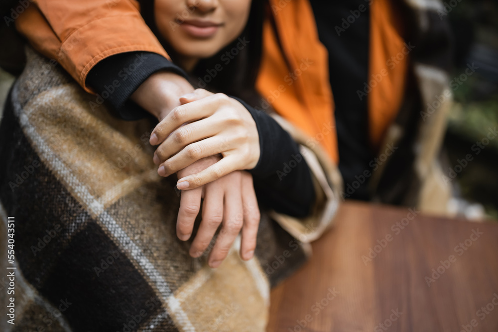 Cropped view of woman in blanket holding hand of boyfriend in outdoor cafe.