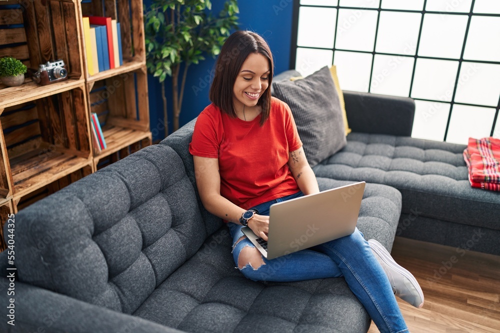 Young beautiful hispanic woman using laptop sitting on sofa at home Young beautiful hispanic woman using laptop sitting on sofa at home