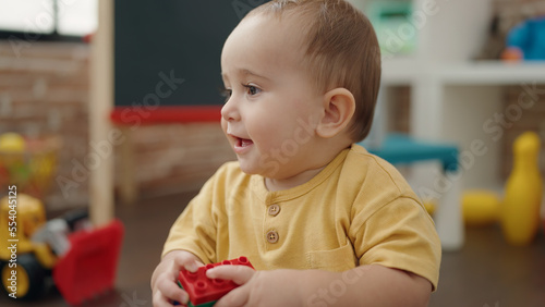 Adorable hispanic baby playing with construction blocks sitting on floor at kindergarten