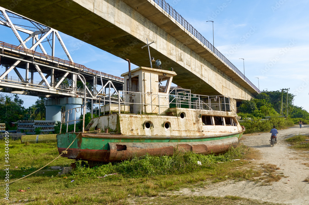 Old boat berthed below river bridge