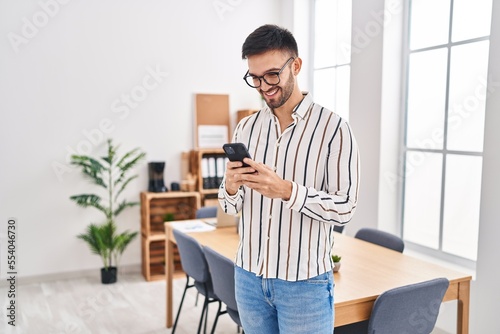 Young hispanic man business worker smiling confident using smartphone at office