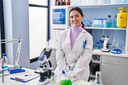 Young brunette woman working at scientist laboratory looking away to side with smile on face, natural expression. laughing confident.