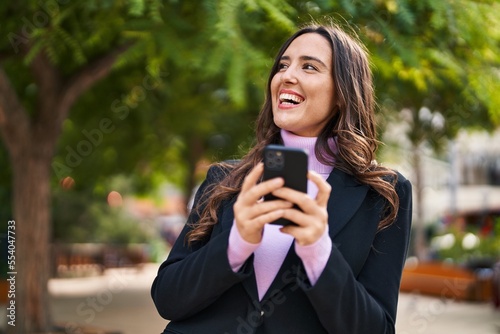 Young hispanic woman smiling confident using smartphone at park