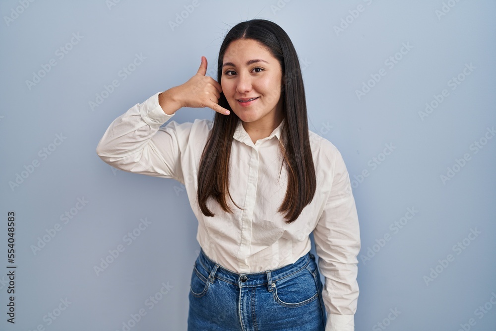 Young latin woman standing over blue background smiling doing phone gesture with hand and fingers like talking on the telephone. communicating concepts. Young latin woman standing over blue background smiling doing phone gesture with hand and fingers like talking on the telephone. communicating concepts.