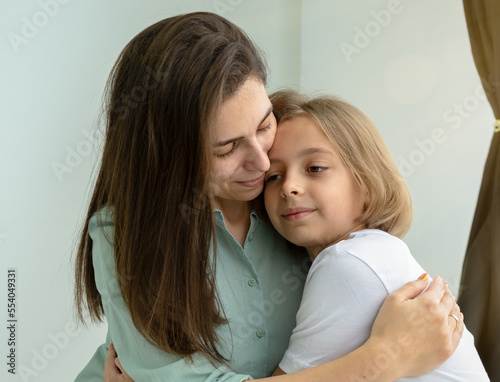 Perfect day together. Portrait of caring mother hugging her daughter at home. They are showing their affection with smile and joy.