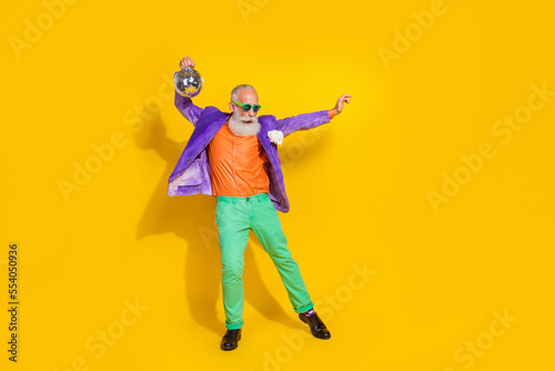 Full length photo of attractive charming guy dressed violet velvet jacket dancing holding disco ball isolated yellow color background