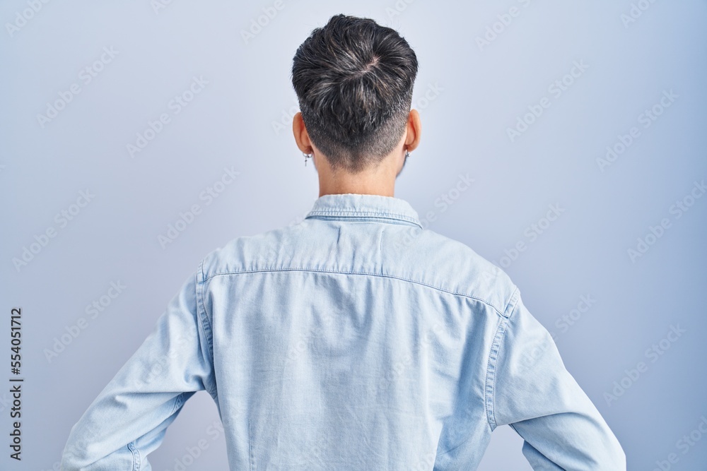 Young hispanic man with beard standing over blue background standing backwards looking away with arms on body Young hispanic man with beard standing over blue background standing backwards looking away with arms on body