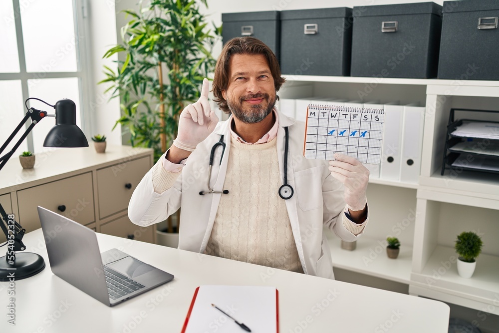 Εκτύπωση καμβά Handsome middle age doctor man holding holidays calendar surprised with an idea