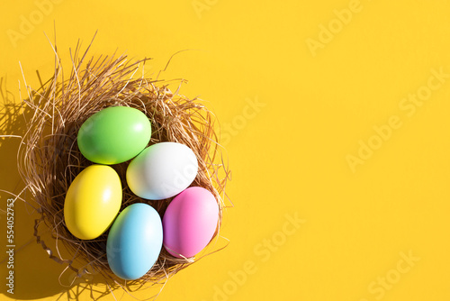 Colorful Easter eggs in a nest on a yellow background. Easter concept. Flat lay, top view, copy space.