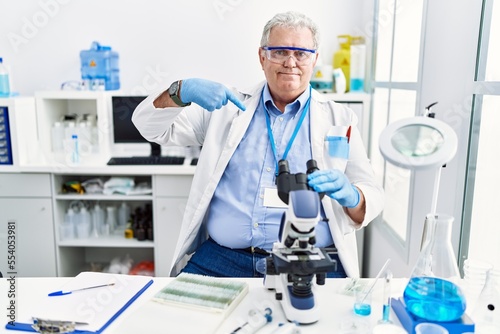 Senior caucasian man working at scientist laboratory looking confident with smile on face  pointing oneself with fingers proud and happy.