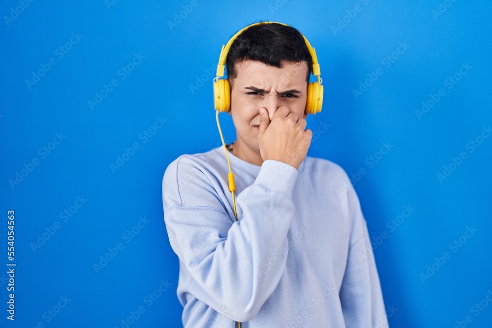 Non binary person listening to music using headphones smelling something stinky and disgusting