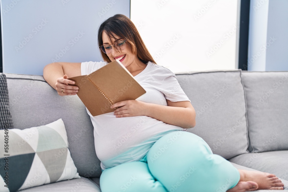 Young pregnant woman reading book sitting on sofa at home Young pregnant woman reading book sitting on sofa at home