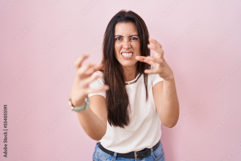 Young brunette woman standing over pink background shouting frustrated with rage, hands trying to strangle, yelling mad Young brunette woman standing over pink background shouting frustrated with rage, hands trying to strangle, yelling mad