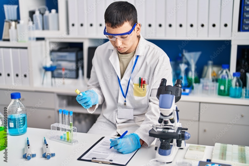 Young man scientist writing on document measuring liquid at laboratory Young man scientist writing on document measuring liquid at laboratory