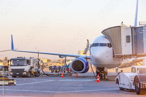 Passenger plane parked at the airport. Refueling operation in action during sunset. Fuel kerosene tanker vehicle. Handling and preparing for departure. Aircraft ground maintenance, pre flight service.