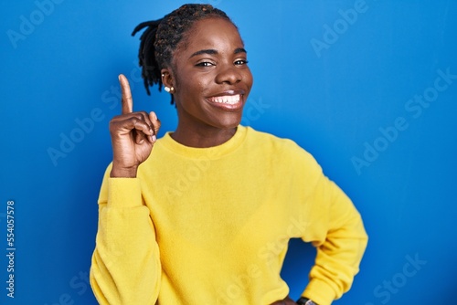 Beautiful black woman standing over blue background pointing finger up with successful idea. exited and happy. number one.