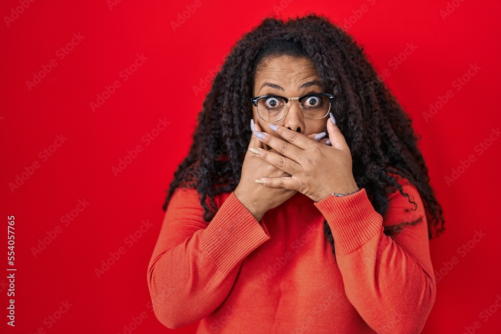 Plus size hispanic woman standing over red background shocked covering mouth with hands for mistake. secret concept. Plus size hispanic woman standing over red background shocked covering mouth with hands for mistake. secret concept.