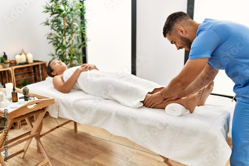 Latin man and woman wearing physiotherapy uniform having rehab session massaging legs at beauty center