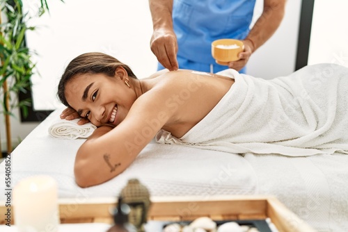Latin man and woman wearing physiotherapy massaging back using salt at beauty center
