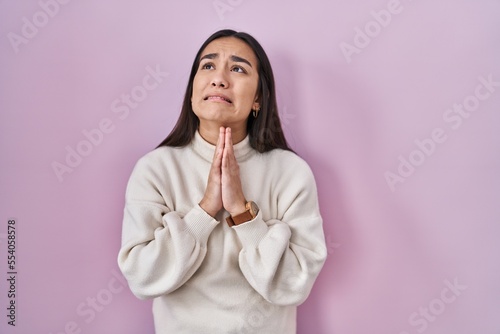 Young south asian woman standing over pink background begging and praying with hands together with hope expression on face very emotional and worried. begging.