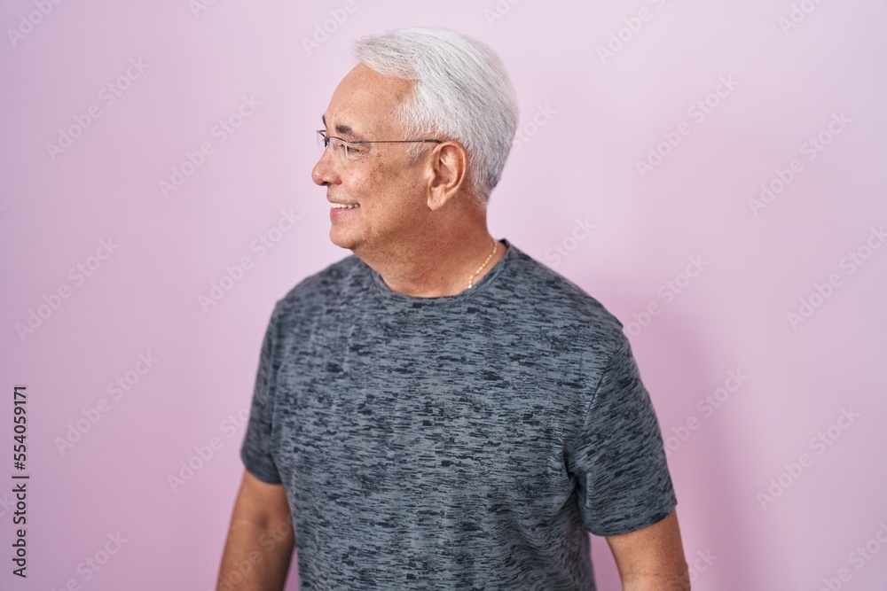 Middle age man with grey hair standing over pink background looking away to side with smile on face, natural expression. laughing confident. Middle age man with grey hair standing over pink background looking away to side with smile on face, natural expression. laughing confident.