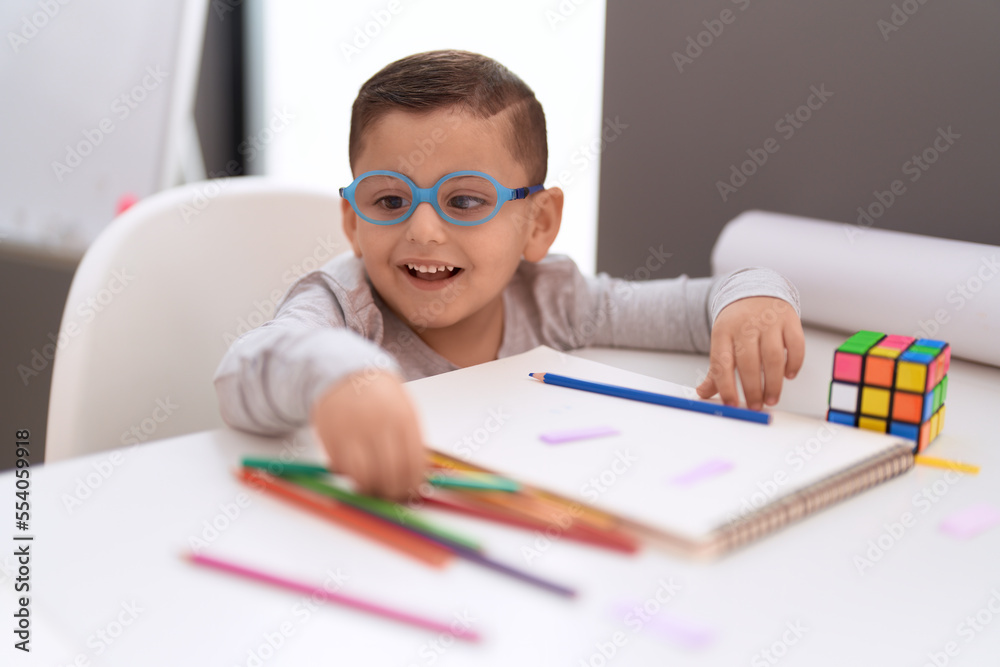 Adorable hispanic toddler student smiling confident drawing on notebook at classroom Adorable hispanic toddler student smiling confident drawing on notebook at classroom