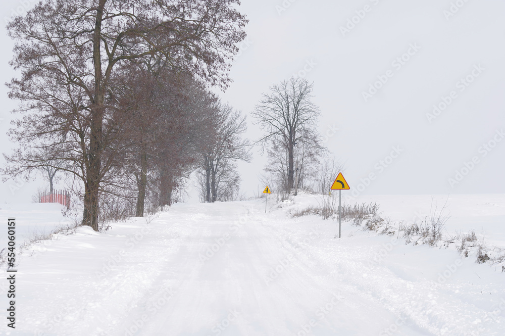 Znak ostrzegawczy, ostry zakręt, zima i ośnieżona droga. Trudne warunki do jazdy. - obrazy, fototapety, plakaty 