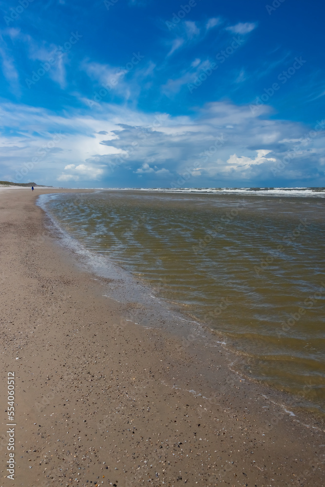 Sandy beach of Wangerooge island on the coast of Germany with shells on the North sea. National park, world natural heritage and perfect place for beachcombing and recreation. Windy day with blue sky.