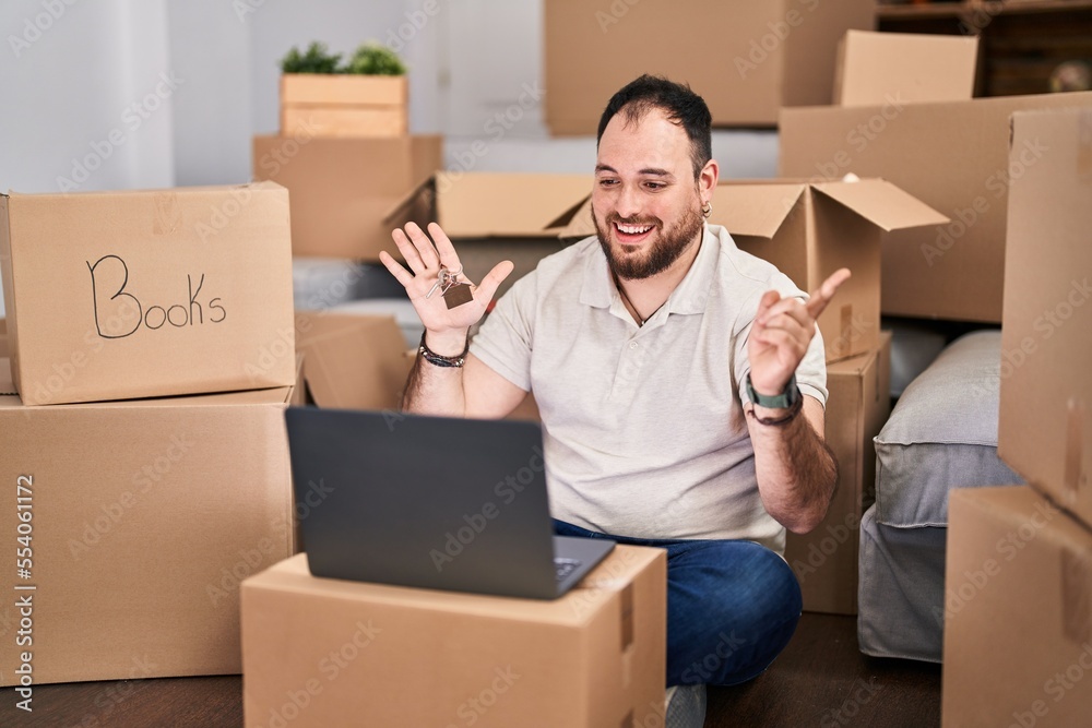 Plus size hispanic man with beard moving to a new home doing video call smiling happy pointing with hand and finger to the side Plus size hispanic man with beard moving to a new home doing video call smiling happy pointing with hand and finger to the side