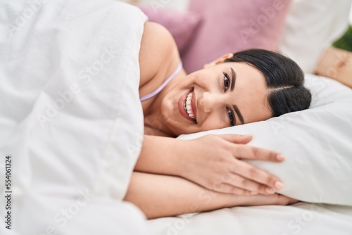 Young hispanic woman smiling confident lying on bed at bedroom