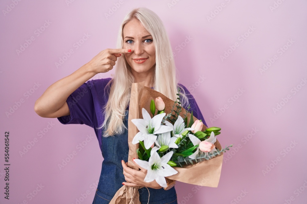 Caucasian woman holding bouquet of white flowers pointing with hand finger to face and nose, smiling cheerful. beauty concept