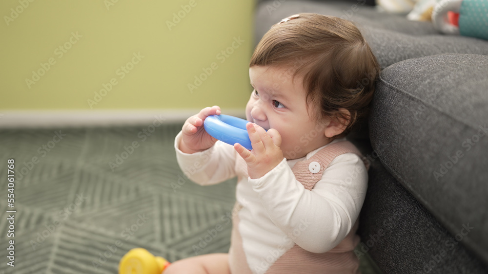 Adorable toddler bitting plastic hoop sitting on floor at home Adorable toddler bitting plastic hoop sitting on floor at home
