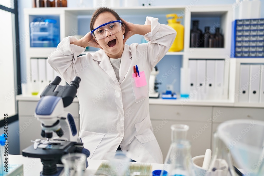 Hispanic girl with down syndrome working at scientist laboratory crazy and scared with hands on head, afraid and surprised of shock with open mouth Hispanic girl with down syndrome working at scientist laboratory crazy and scared with hands on head, afraid and surprised of shock with open mouth