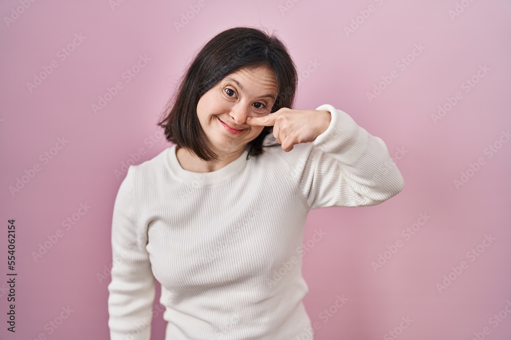 Woman with down syndrome standing over pink background pointing with hand finger to face and nose, smiling cheerful. beauty concept Woman with down syndrome standing over pink background pointing with hand finger to face and nose, smiling cheerful. beauty concept