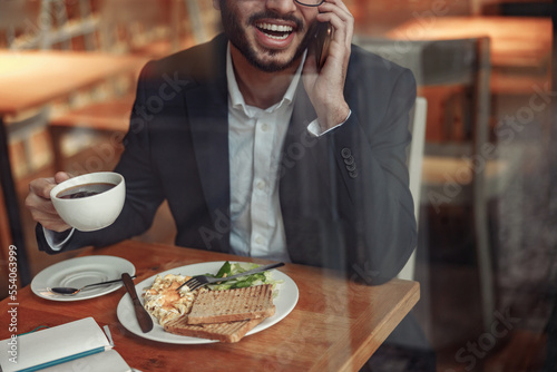 Close up of indian businessman is talking phone with client during lunch time in cozy cafe