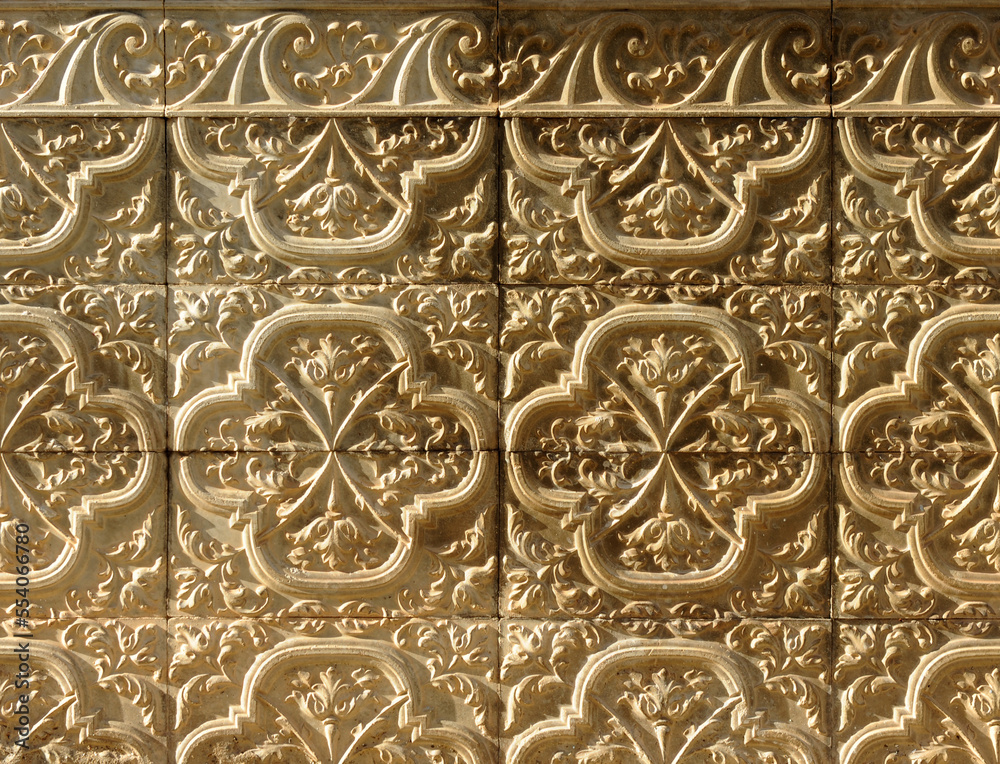 Background with grazing lighting of ceramic terracotta tiles with floral and serlian motifs in relief on the socle of a Spanish house. Decorative architectural background for facades