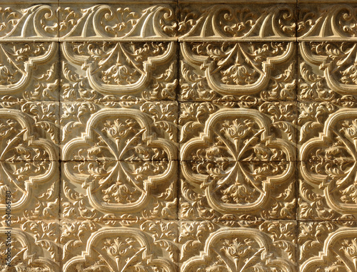 Background with grazing lighting of ceramic terracotta tiles with floral and serlian motifs in relief on the socle of a Spanish house. Decorative architectural background for facades