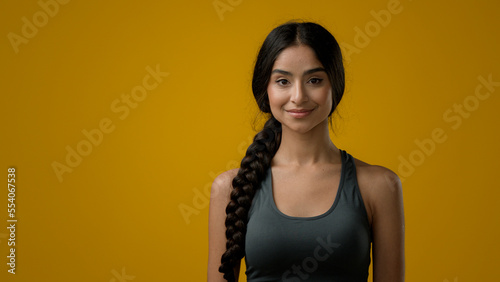 Calm casual sporty 20s Indian Ethnic multiracial woman with long braid hairstyle posing standing in yellow studio background backdrop positive girl ethnicity female lady sport instructor fitness model