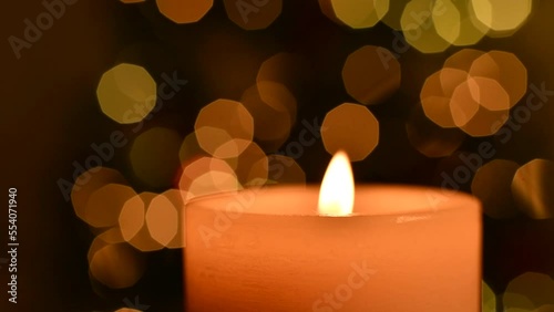 Burning candle close-up on a holiday evening. Festive candlelight with tranquil bokeh lights on dark background.