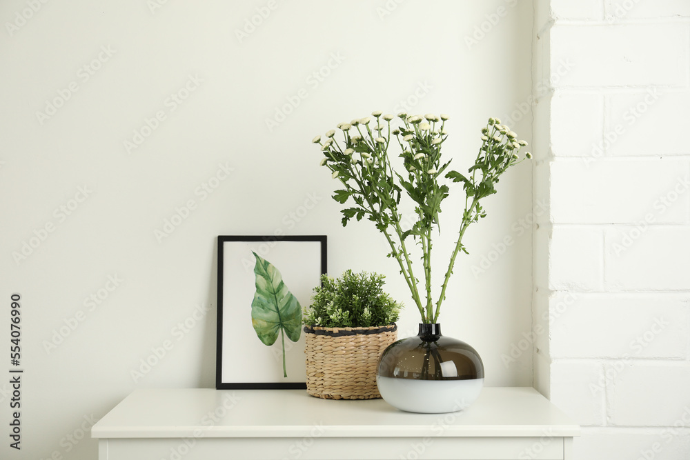 Fototapeta premium Decorative vase with flowers and houseplant on commode indoors