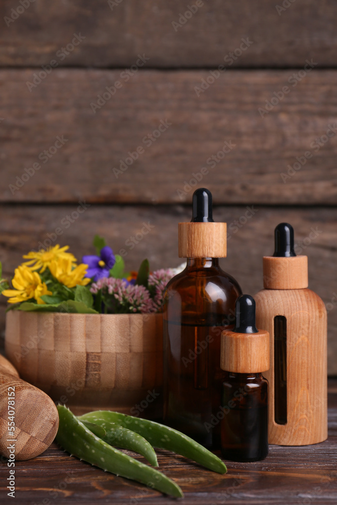 Glass bottles of aromatic essential oil and mortar with different herbs on wooden table