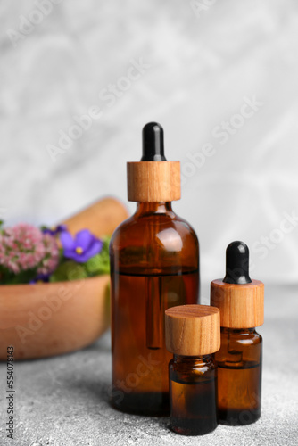 Glass bottles of essential oil and mortar with different wildflowers on light grey table