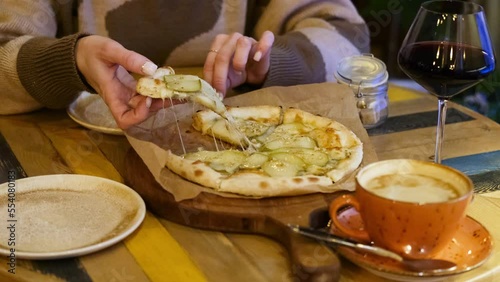 A woman's hand takes a piece of hot pizza with pear and cheese, sitting in a cafe in the evening. photo