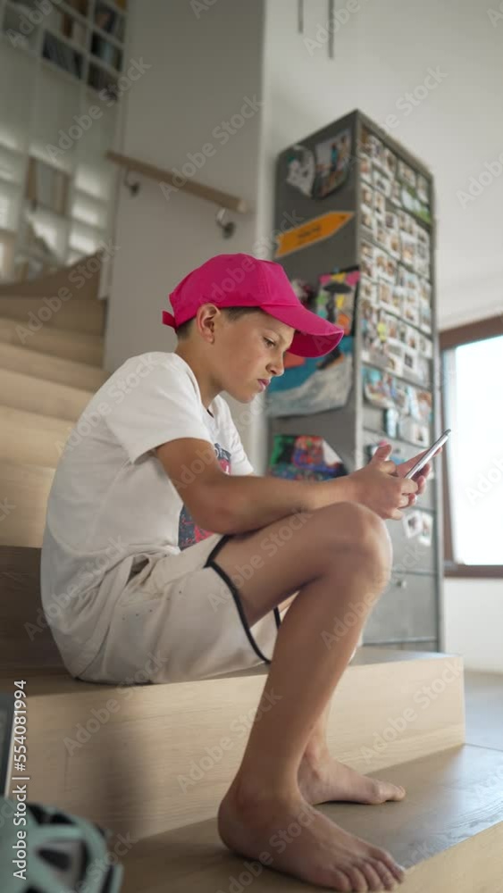One young boy scrolling social media on smartphone device at home sitting by staircases. Teen kid using phone looking at screen in Vertical Video One young boy scrolling social media on smartphone device at home sitting by staircases. Teen kid using phone looking at screen in Vertical Video